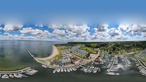 Une vue aérienne d’une marina où sont amarrés des bateaux, d’une plage de sable et d’une petite ville avec des bâtiments et de la végétation.