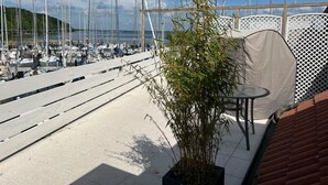 Un port de plaisance où sont amarrés de nombreux voiliers, un bambou en pot et un espace de repos abrité avec une table et des chaises.