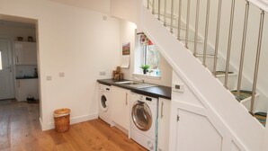 A compact kitchen with a washing machine, a sink, and a window with a view of greenery. - Taorbeag at Taormina (Fort William)
