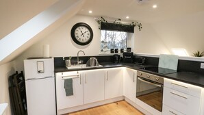 A modern kitchen with white cabinets, a black countertop, a clock, and a window with a view of trees. - Taorbeag at Taormina (Fort William)