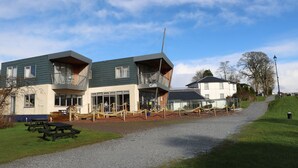 A two-story building with a café on the ground floor, outdoor seating, and a gravel path leading to the entrance. - Taorbeag at Taormina (Fort William)