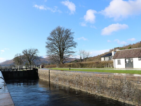 A stone lock gate, a grassy area, and a building with a tiled roof.