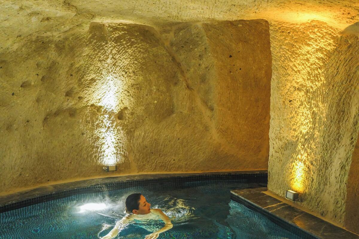 Eine Person schwimmt in einem Pool mit einer reliefartigen Steinwand und einer kleinen Wandleuchte.