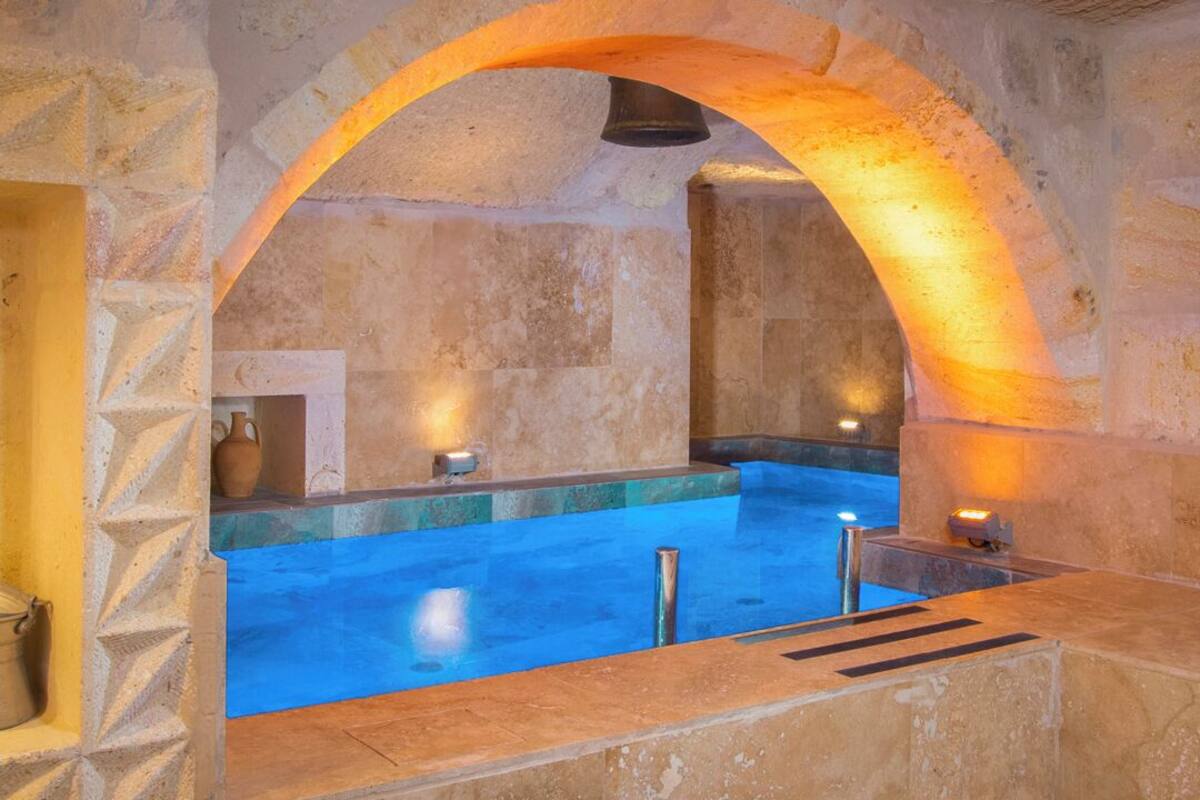 Ein Innenpool mit Steinwänden, einem blauen Wasserspiel, einer Steinsitzbank und einem steinernen Bogen.