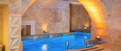 A stone-walled indoor pool with a blue water feature, a stone bench, and a stone archway.