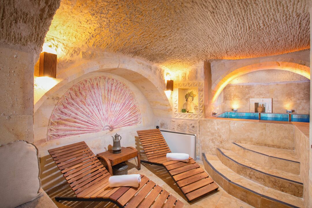 A spa with wooden loungers, a stone wall with a fan, and a pool area.