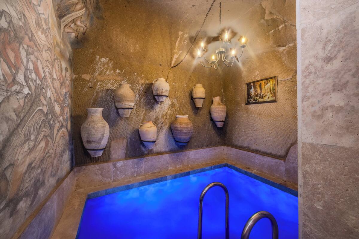 Ein Zimmer mit steinernen Wänden, einem blauen Pool, Wandvasen und einem Kronleuchter.