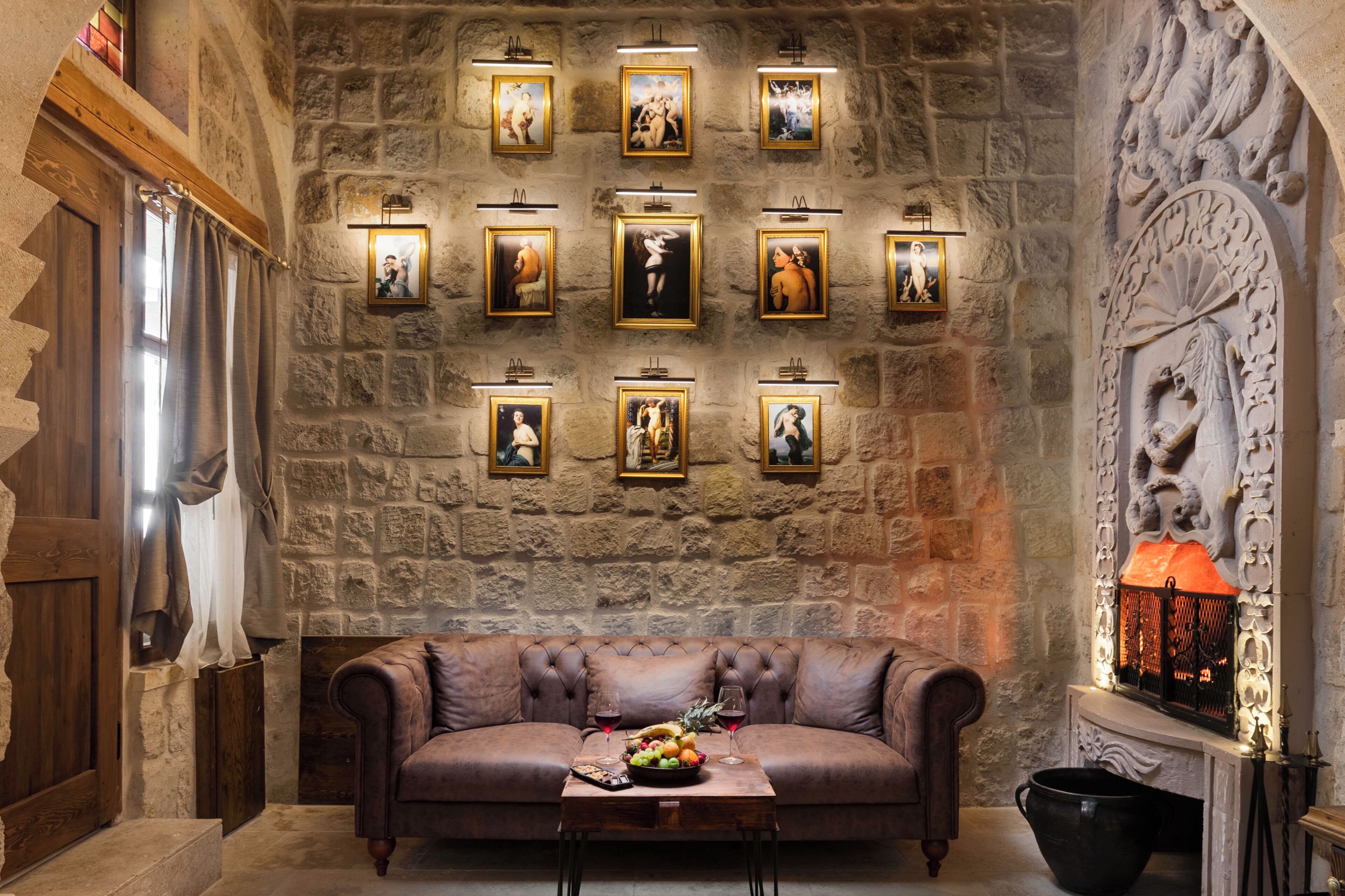 Una habitación con paredes de piedra, un sofá de cuero, una mesa con fruta y copas de vino, y cuadros en la pared.