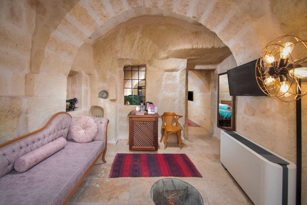 Ein Zimmer mit Steinsäulen, einer Couch, einem Holzstuhl, einem kleinen Tisch mit Gegenständen, einem Heizkörper und einem Fernseher.