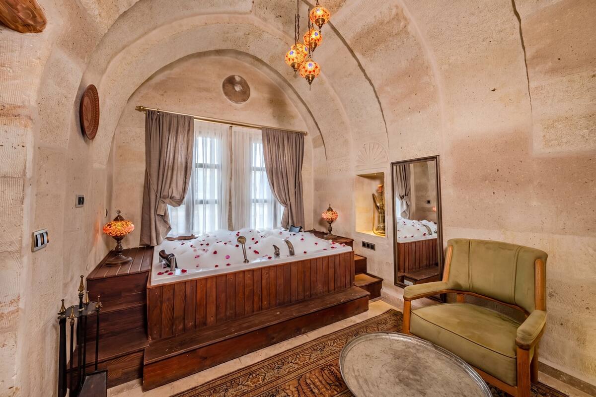 Ein Zimmer mit einer Holzbadewanne, einem grünen Sessel, einem Spiegel und einem gemusterten Teppich.