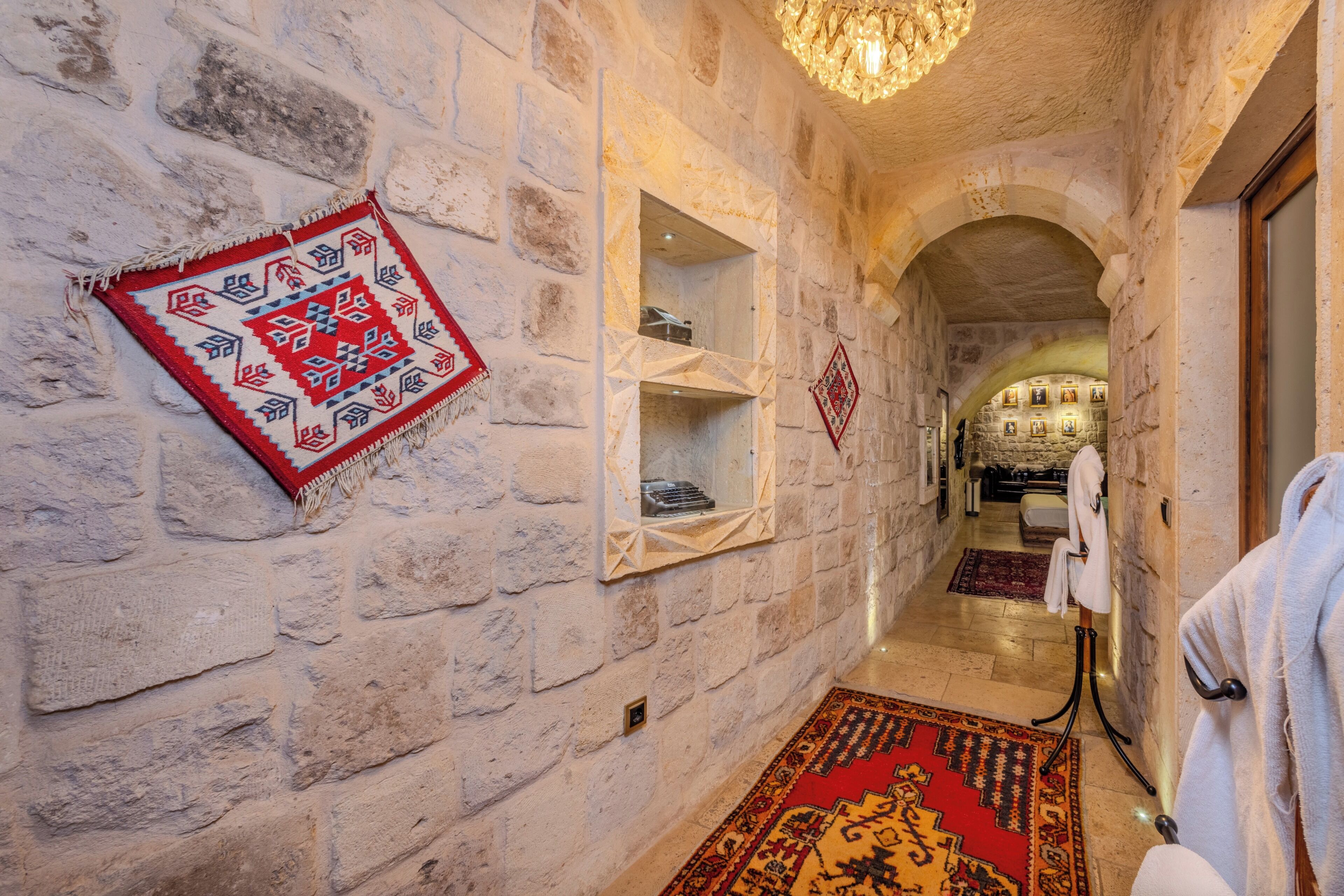 Un couloir aux murs de pierre, agrémenté d’un lustre, d’un tapis à motifs et d’un porte-serviettes.