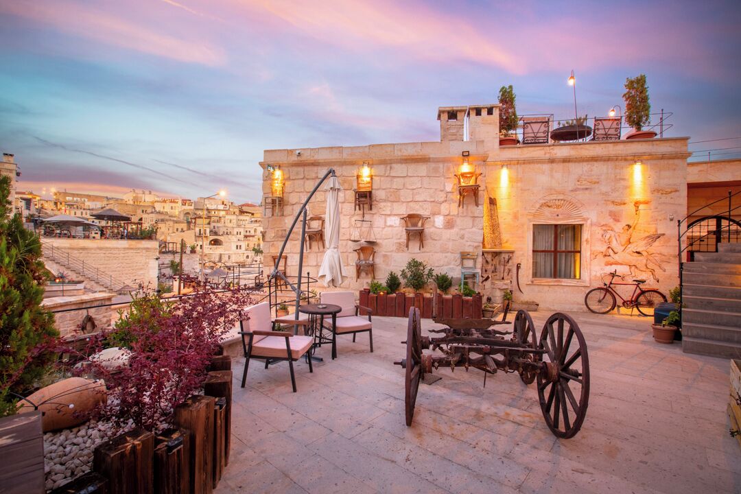 A rooftop patio with outdoor seating, a bicycle, and a stone building with a mural.