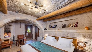 A rustic room with a fireplace, wooden beams, a bed with a teal bedspread, and a shelf with books and a mirror.
