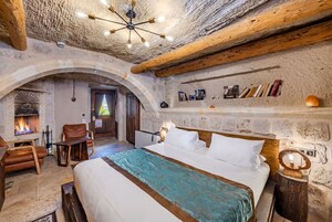Una habitación rústica con chimenea, vigas de madera, una cama con colcha color turquesa y una estantería con libros y un espejo.