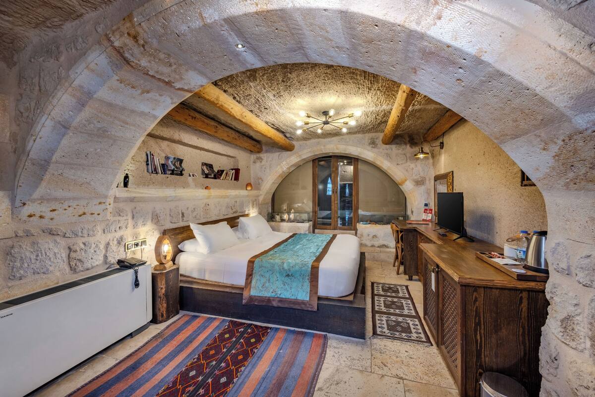 Ein gemütliches Zimmer mit einem Bett, einem Holztisch, einem Fernseher und einer Steinwand.
