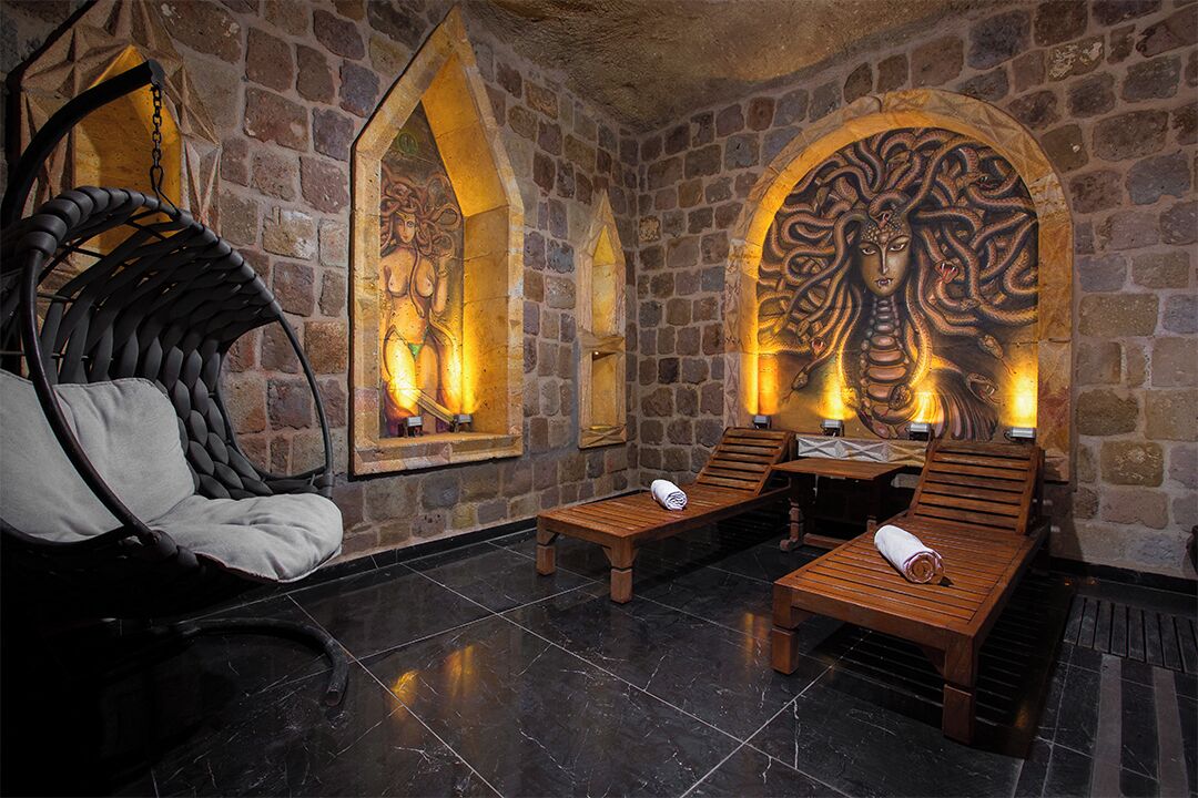 Una habitación con paredes de piedra, una silla de hierro forjado, sillones de madera y un mural.