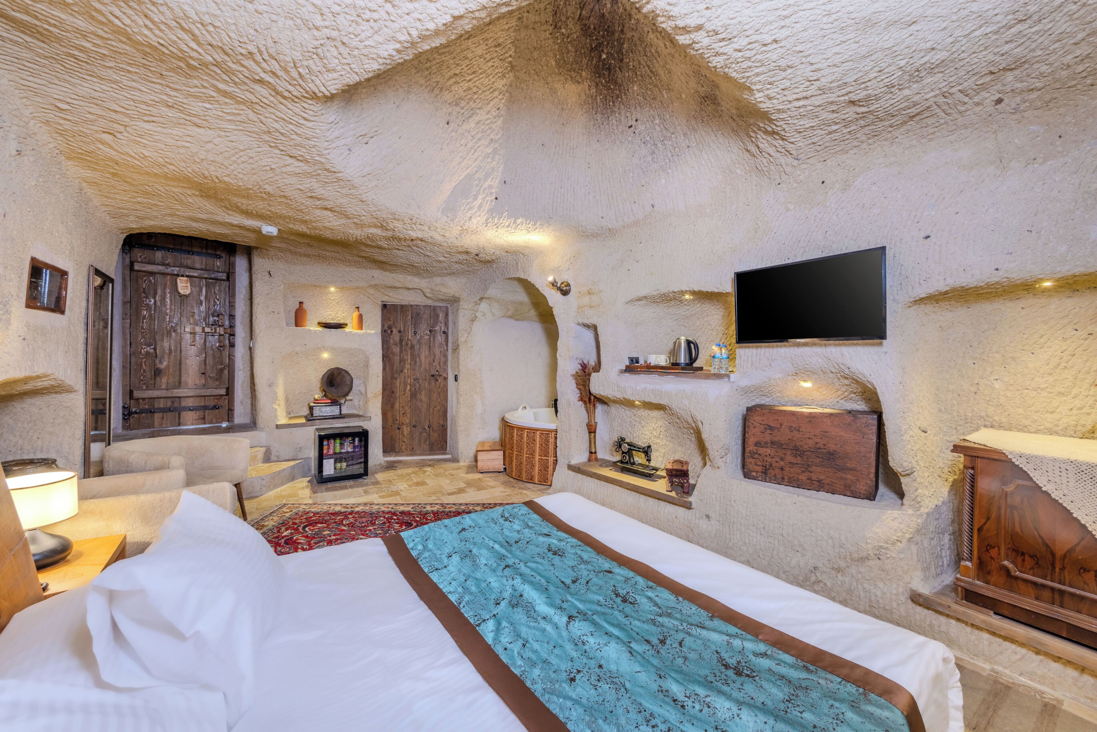 A cozy room with a bed, a wooden door, a television, and a shelf with decorative items.