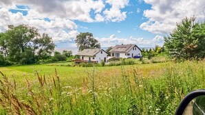 A rural setting with two white houses, a grassy field, and a clear sky.