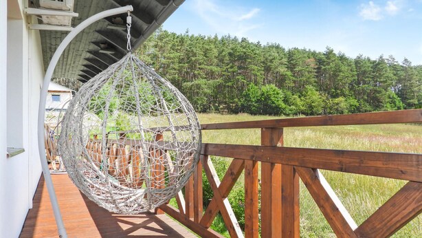A wooden deck with a hanging wicker chair and a view of a forested area.