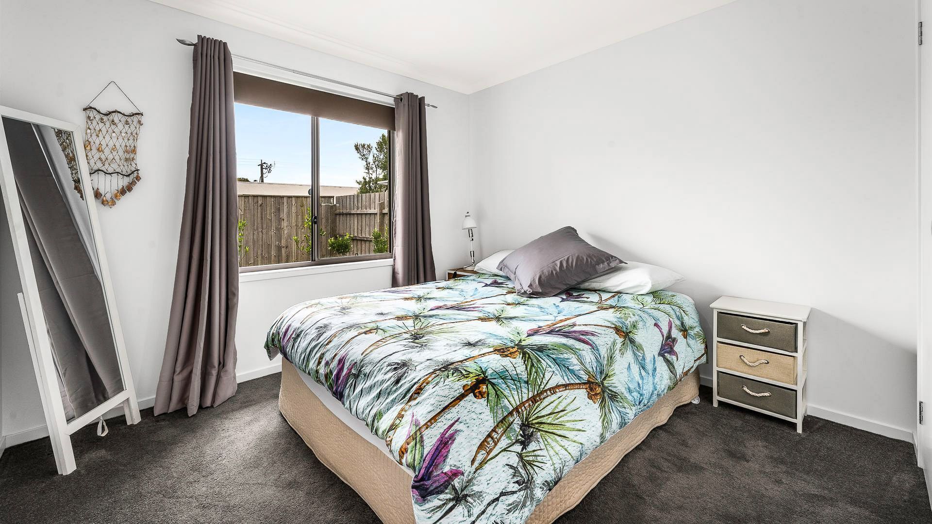 Un dormitorio con cama, mesita de noche, cortinas en la ventana, decoración en la pared y vistas al exterior.