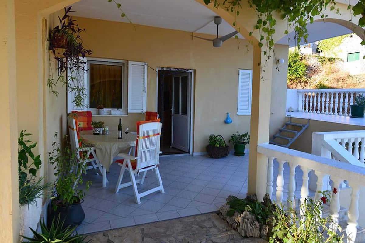 An outdoor patio with a table and chairs, a ceiling fan, and a staircase leading to an upper level.