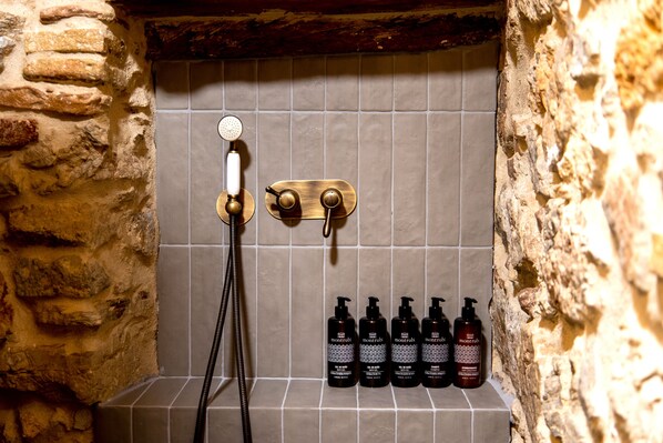 A shower area with a stone wall, a showerhead, and a shelf with bottles.