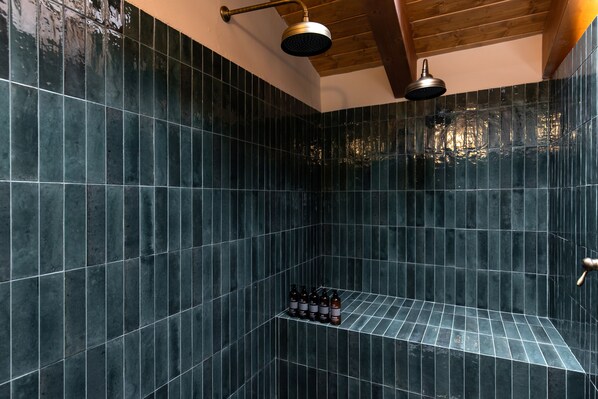 Une salle de bain moderne avec des carreaux foncés, une pomme de douche et une étagère remplie de bouteilles.
