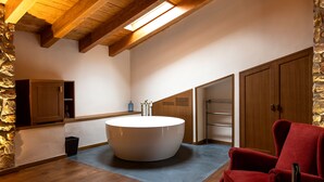 A modern bathroom with a large bathtub, wooden beams, stone walls, and a red chair. - Hotel Montrubí 1771 - Slow Winery Hotel - Adults only (Font-Rubi)