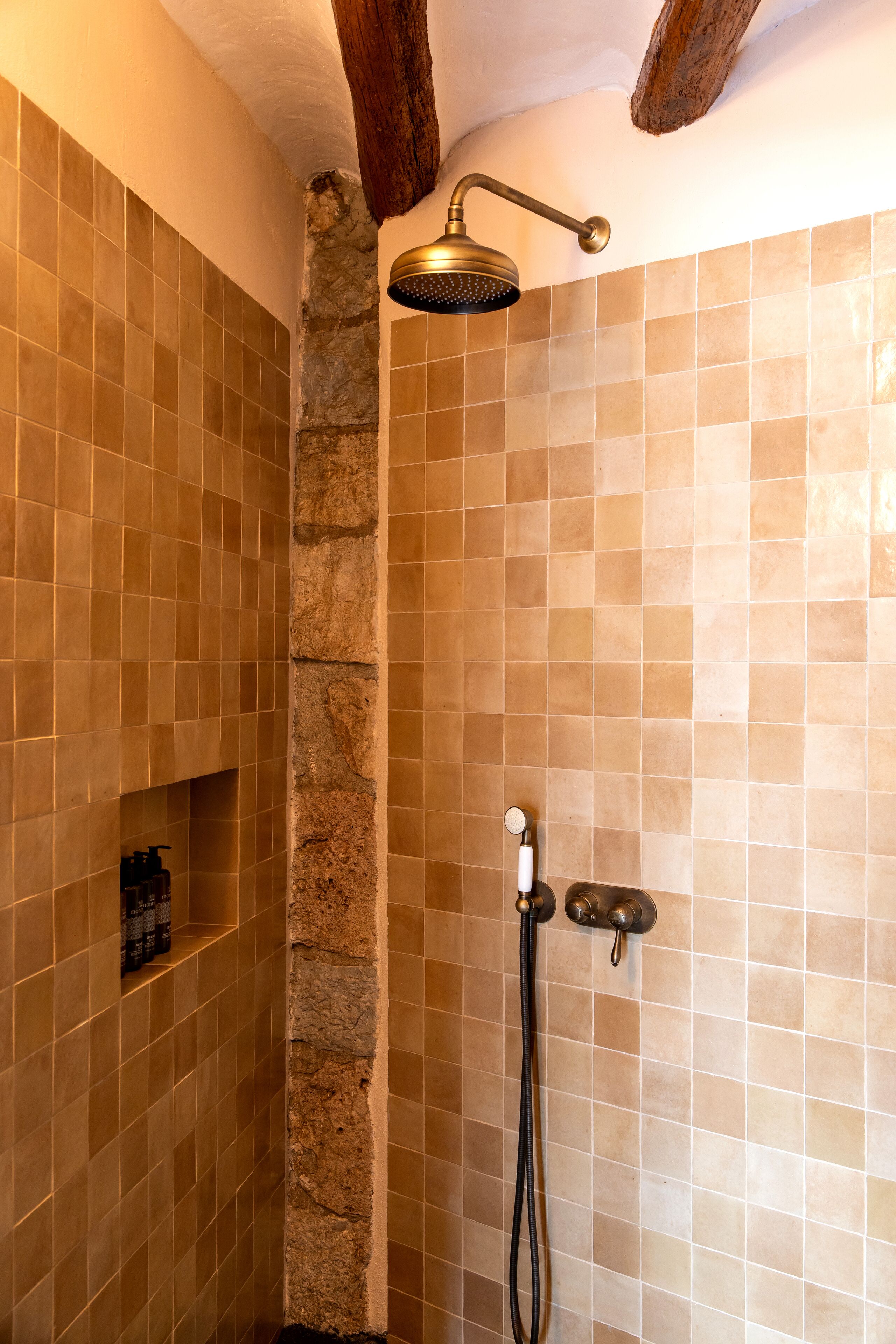 Ducha con detalles de pared de piedra, cabezal de ducha de mano y grifo empotrado.