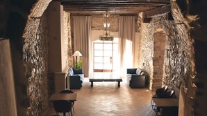 A stone-walled corridor with a wooden bench, tables, and chairs, leading to a room with a window and a lamp. - Hotel Montrubí 1771 - Slow Winery Hotel - Adults only (Font-Rubi)