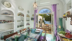 A dining area with a table set for four, surrounded by shelves with decorative plates and a view of the outdoors. - Casa del Fico Dimora storica Positano (Positano)