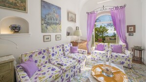 A room with a floral sofa set, a wooden cabinet, and a view through an arched window. - Casa del Fico Dimora storica Positano (Positano)