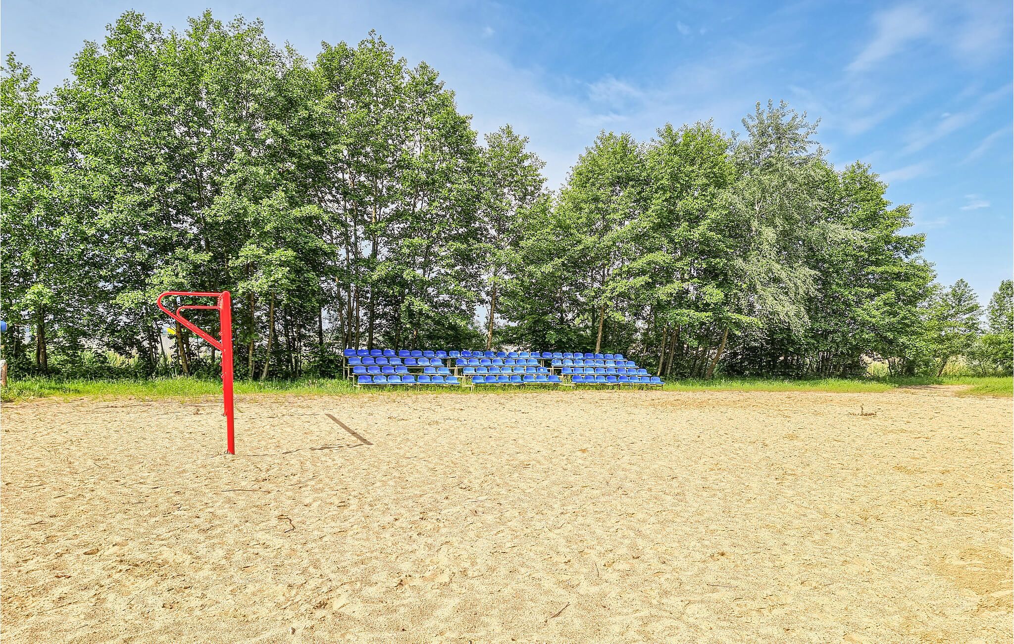 A sandy sports field with blue stadium seating and a red goalpost.