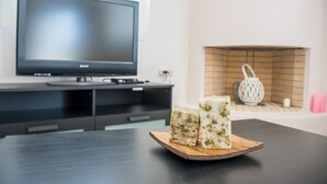 Uma sala de estar moderna com uma TV de tela plana, lareira e uma mesa de madeira com dois pedaços de queijo.