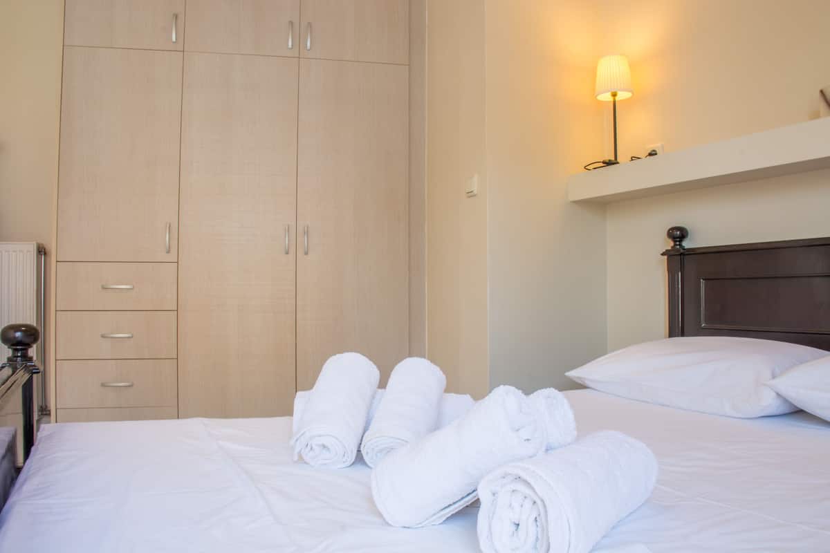 A hotel room with a bed, white linens, a wooden wardrobe, and a wall-mounted lamp.