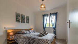 A bedroom with a wooden headboard, a patterned bedspread, a bedside lamp, and a hanging light fixture.