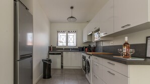 A modern kitchen with stainless steel appliances, a window with a curtain, and a countertop with a bottle and glasses.
