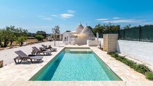 A swimming pool with lounge chairs, a stone building with conical roofs, and a clear blue sky.