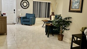 A living room with a blue armchair, a round table, a potted plant, and a framed picture on the wall. -  Spacious 1-bedroom just mins to  WEF  (Wellington)