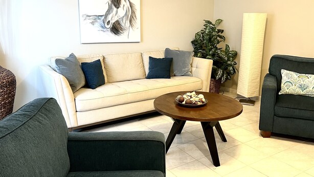 A living room with a beige sofa, a dark armchair, a round coffee table, and a large potted plant. -  Spacious 1-bedroom just mins to  WEF  (Wellington)