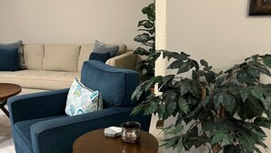 A living room with a blue sofa, a round wooden coffee table, and a large potted plant. -  Spacious 1-bedroom just mins to  WEF  (Wellington)