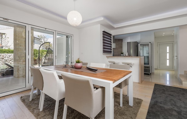 Un espace repas moderne avec une table en bois, des chaises blanches et un luminaire suspendu.