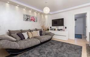 Un salon moderne comprenant un canapé, un téléviseur à écran plat, un élément décoratif mural et un luminaire au plafond.