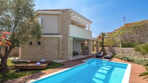 Uma casa moderna de dois andares com piscina, área de estar externa e muro de pedra.