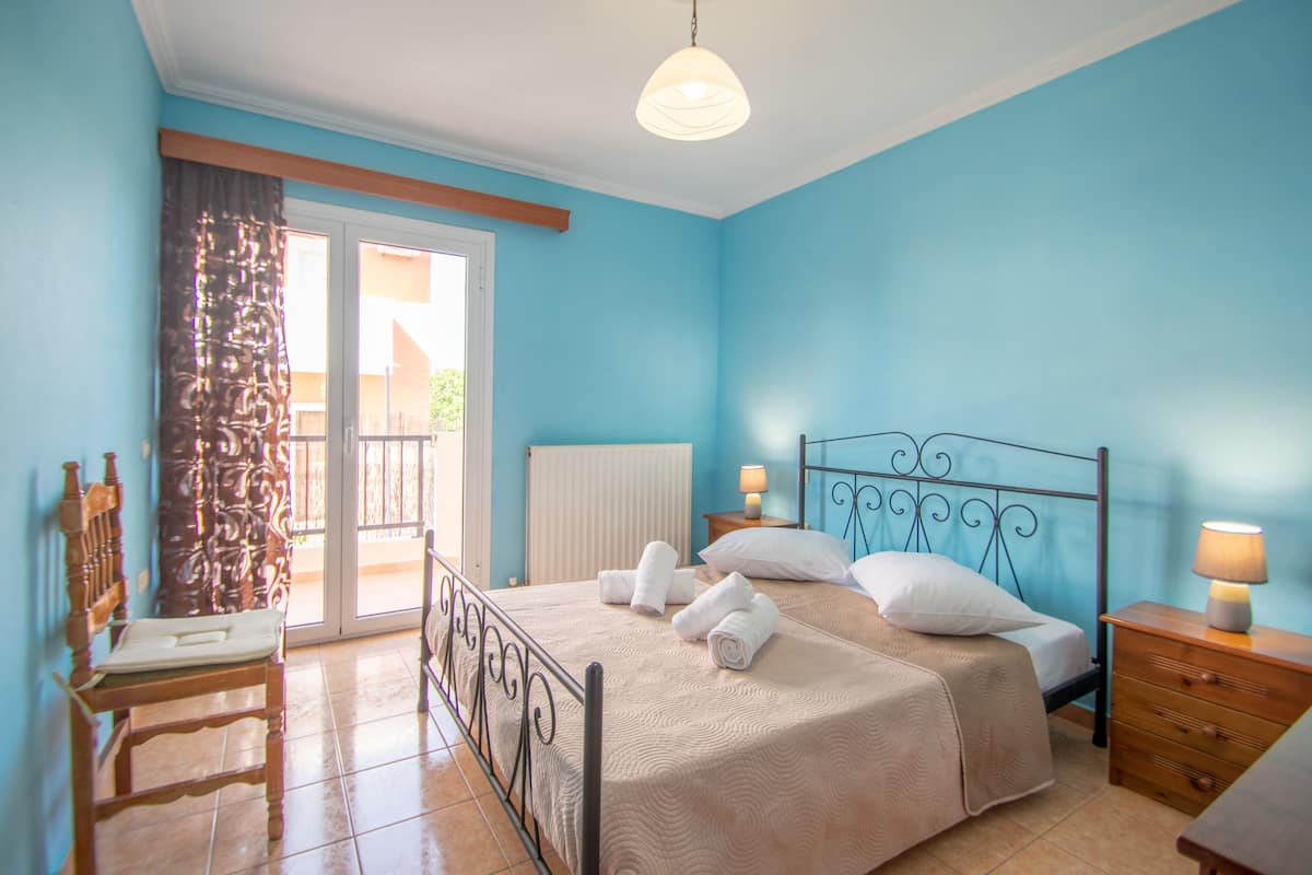 Une chambre à coucher avec un lit, deux tables de chevet, une chaise et une fenêtre avec des rideaux.