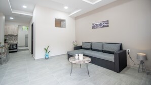 Ein modernes Wohnzimmer mit einer Couch, einem kleinen runden Tisch und einer Küche im Hintergrund.
