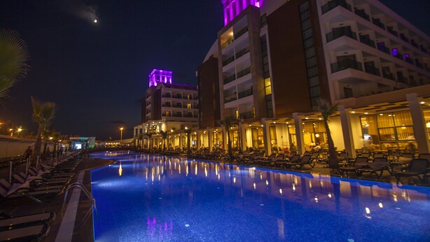 Uma área de piscina de hotel com espreguiçadeiras e uma piscina grande que reflete as luzes do edifício.