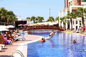 A swimming pool with lounge chairs and umbrellas, surrounded by palm trees and a building. - Linda Sunny Beach Hotel & Spa-Ultra All Inclusive (Manavgat)