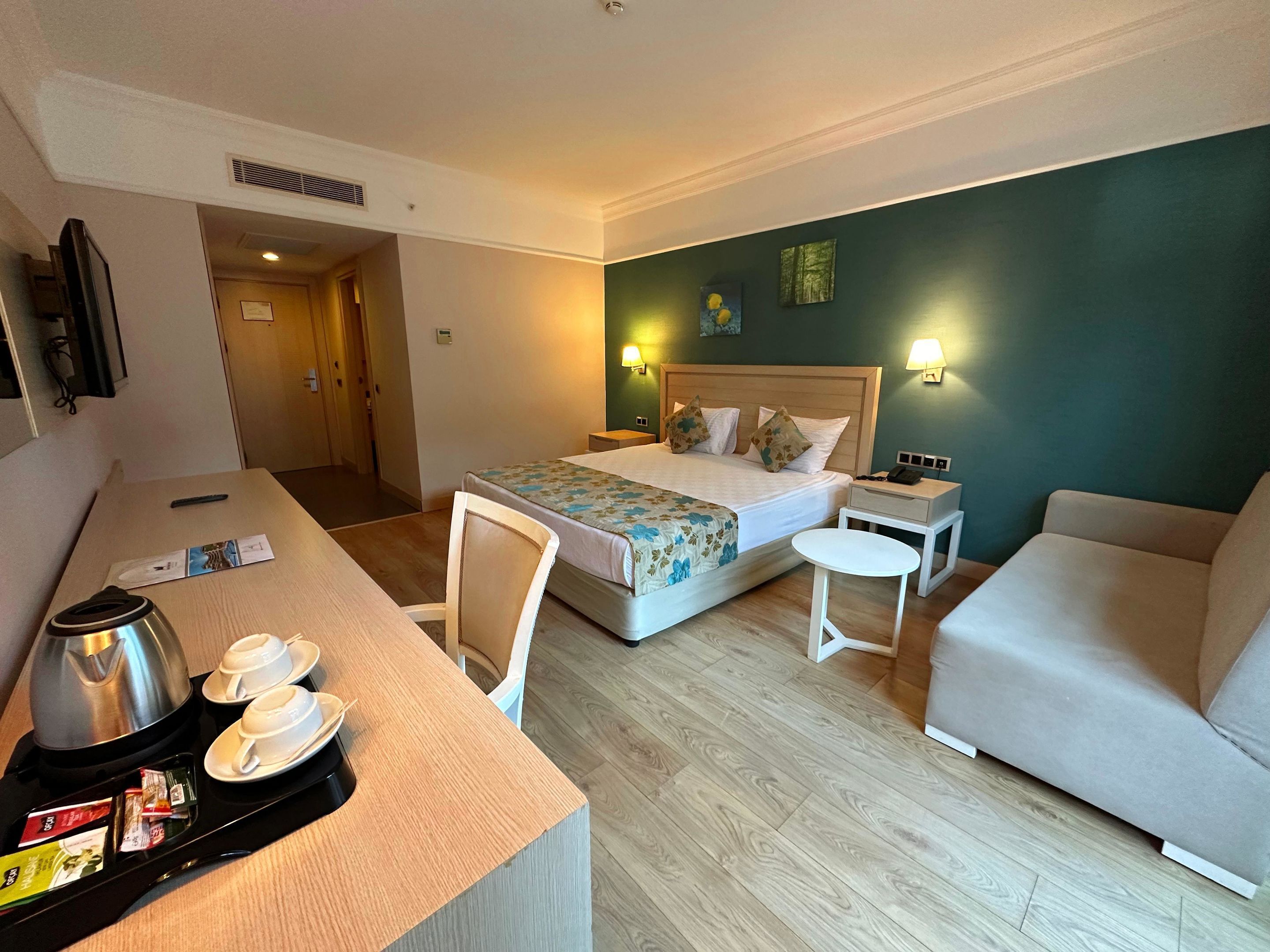 Une chambre d’hôtel comprenant un lit, deux tables de chevet, un bureau avec une machine à café et des tasses, une chaise et un canapé.