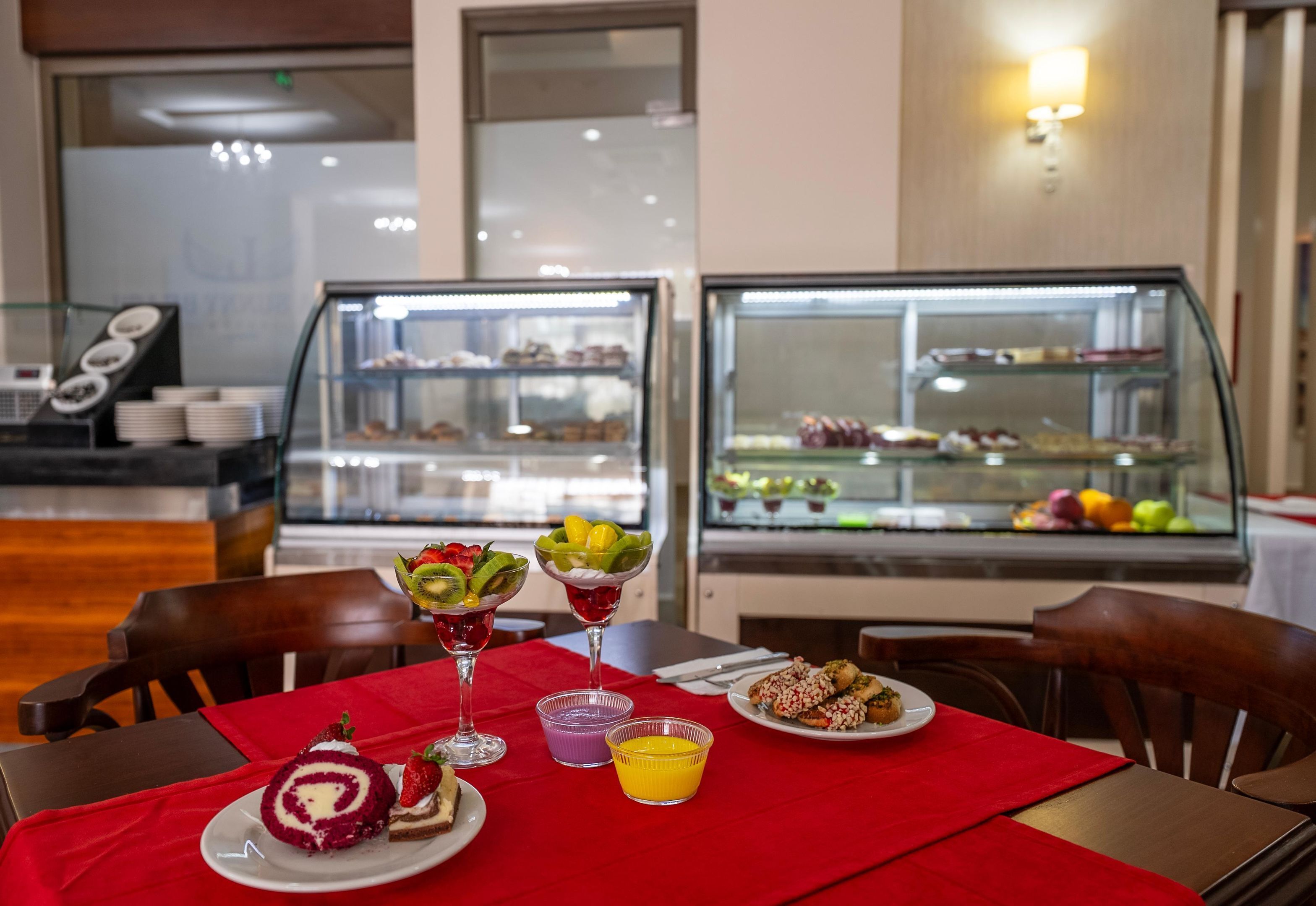 Una mesa de comedor con mantel rojo, diversos postres y un frutero.